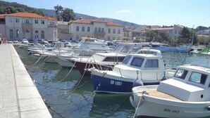 A marina with several boats docked, a paved walkway, and buildings with red roofs in the background. - Rab Oasis Retreat - 3 Bedroom Apartment (Rab)