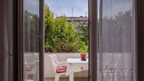 A balcony with a table and chairs, a potted plant, and a view of a building and trees. - Rab Oasis Retreat - 3 Bedroom Apartment (Rab)