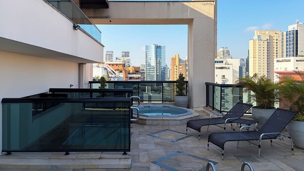 A rooftop terrace with a glass balustrade, a hot tub, and lounge chairs. - Apartamento Conforto - Itaim Bibi (São Paulo)