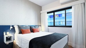 A hotel room with a bed, bedside table, phone, and a window with curtains. - Apartamento Conforto - Itaim Bibi (São Paulo)