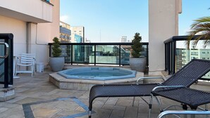 A rooftop terrace with a hot tub, lounge chairs, potted plants, and a view of the cityscape. - Apartamento Conforto - Itaim Bibi (São Paulo)