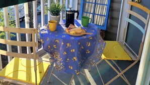 A small outdoor table with a blue tablecloth, a yellow mug, a green mug, a black coffee pot, and a plate with toast. - Cozy Condo Near City Dock - Your Perfect Annapolis Getaway! (Annapolis)
