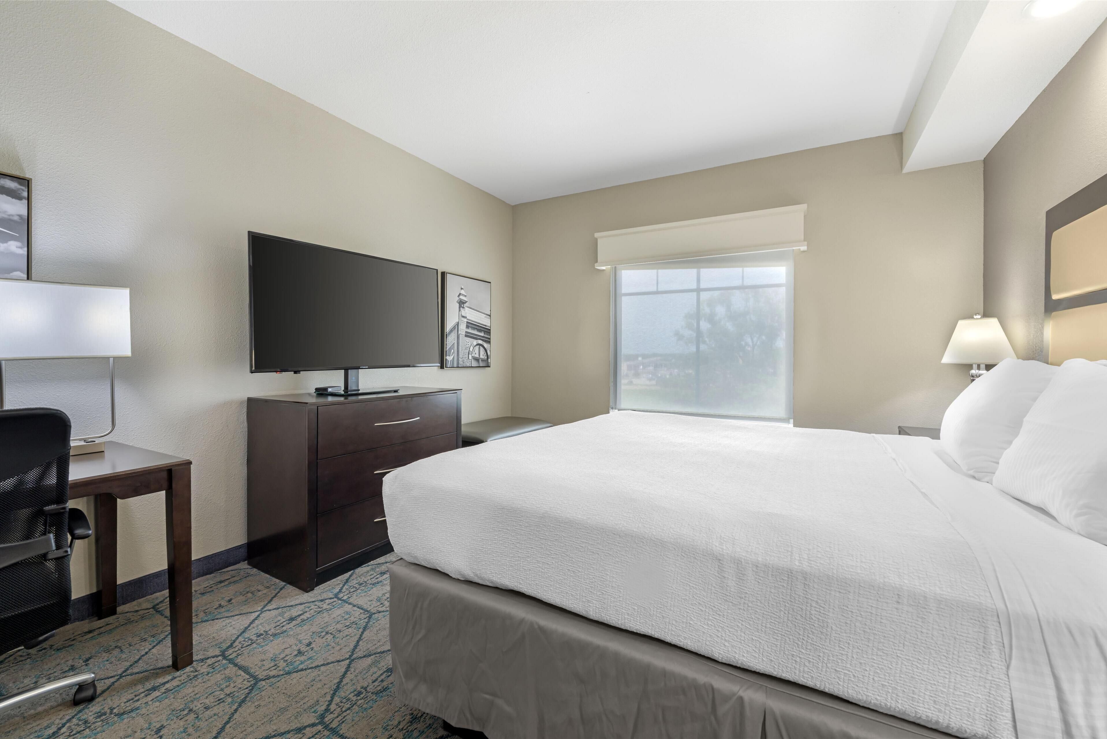 Una habitación de hotel con cama, escritorio, televisión y ventana con vistas.