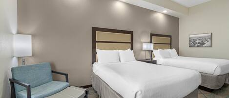 A hotel room with two beds, a chair, a small table, and a lamp.