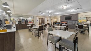 A spacious restaurant with multiple tables and chairs, a counter with a cash register, and a television mounted on the wall. - Best Western Plus McPherson (McPherson)