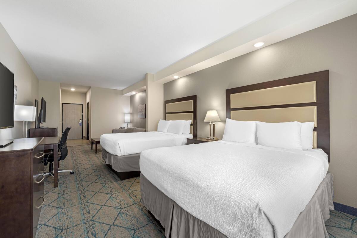 A hotel room with two beds, a desk, a chair, a lamp, and a television.