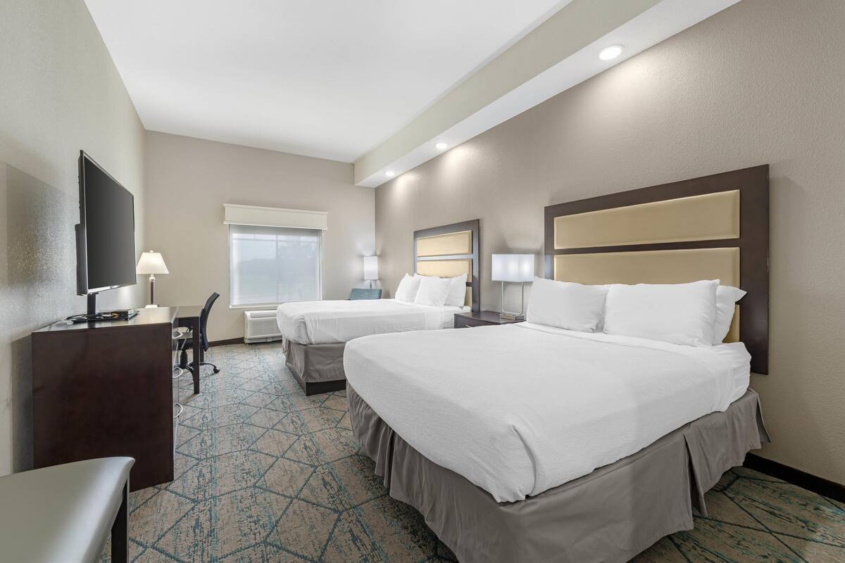 A hotel room with two beds, a desk, a chair, a TV, and a window.