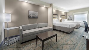 A hotel room with a gray sofa, two beds, a desk, and a patterned carpet. - Best Western Plus McPherson (McPherson)