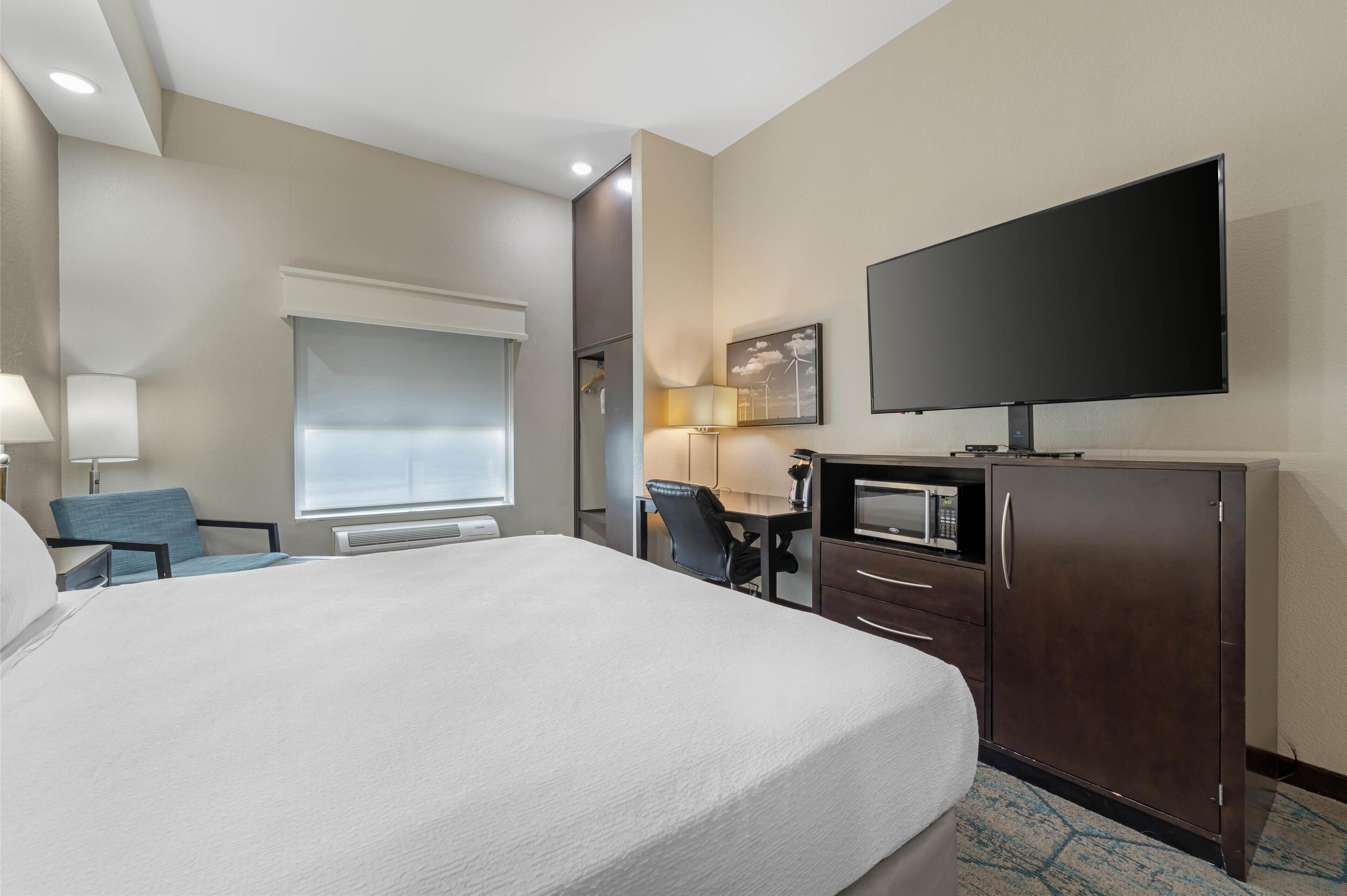 A hotel room with a large bed, a desk with a chair, a television, a microwave, and a wardrobe.