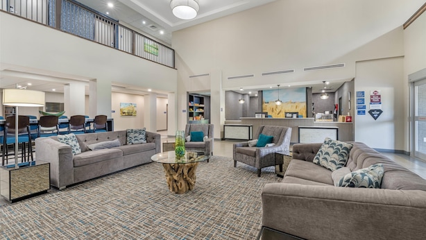 A spacious lobby with a high ceiling, a central seating area with sofas and chairs, a dining area with a bar, and a kitchen visible in the background. - Best Western Plus McPherson (McPherson)