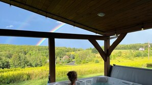 A person in a hot tub with a view of a green landscape and a rainbow. - Custom Finger Lakes home near Ithaca with hot tub  (Newfield)