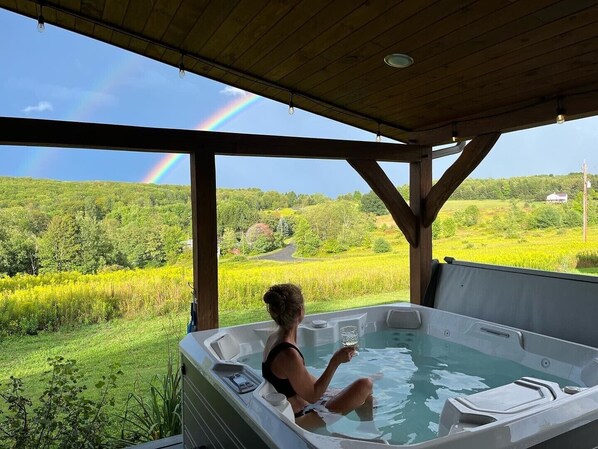 A person in a hot tub with a view of a green landscape and a rainbow. - Custom Finger Lakes home near Ithaca with hot tub (Newfield)