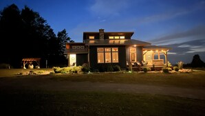 A modern two-story house with a covered porch and a well-lit front yard. - Custom Finger Lakes home near Ithaca with hot tub  (Newfield)