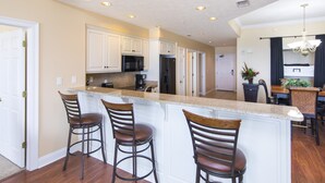 Una cocina con gabinetes blancos, una isla central con taburetes de bar y un comedor con candelabro.