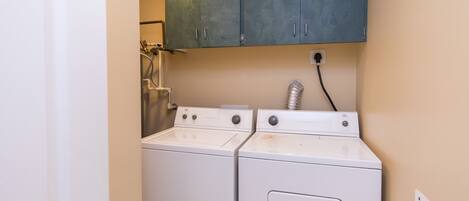 A laundry area with two white washing machines, a metal cabinet above, and a visible electrical outlet.