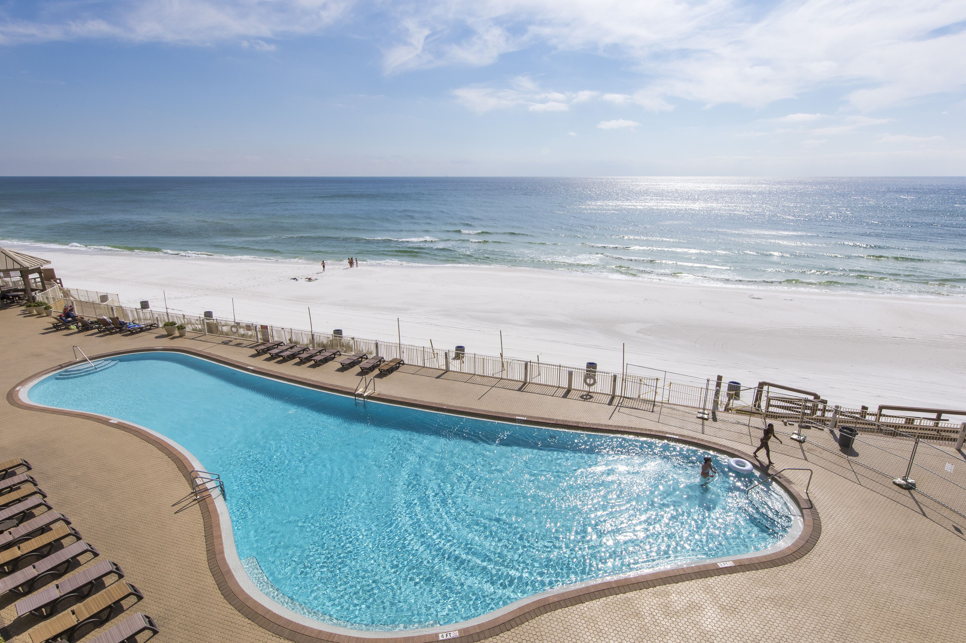 Ein Pool neben einem Strand mit Liegestühlen und einem Zaun.