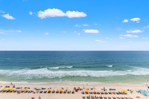 A beach with rows of sun loungers and umbrellas, a clear sky, and the ocean.