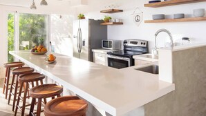 Une cuisine moderne dotée d’un grand îlot central, de tabourets de bar, d’appareils électroménagers en acier inoxydable et d’étagères en bois.