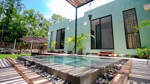 Zona de piscina exterior moderna amb un pont de fusta, seients i plantes en testos.