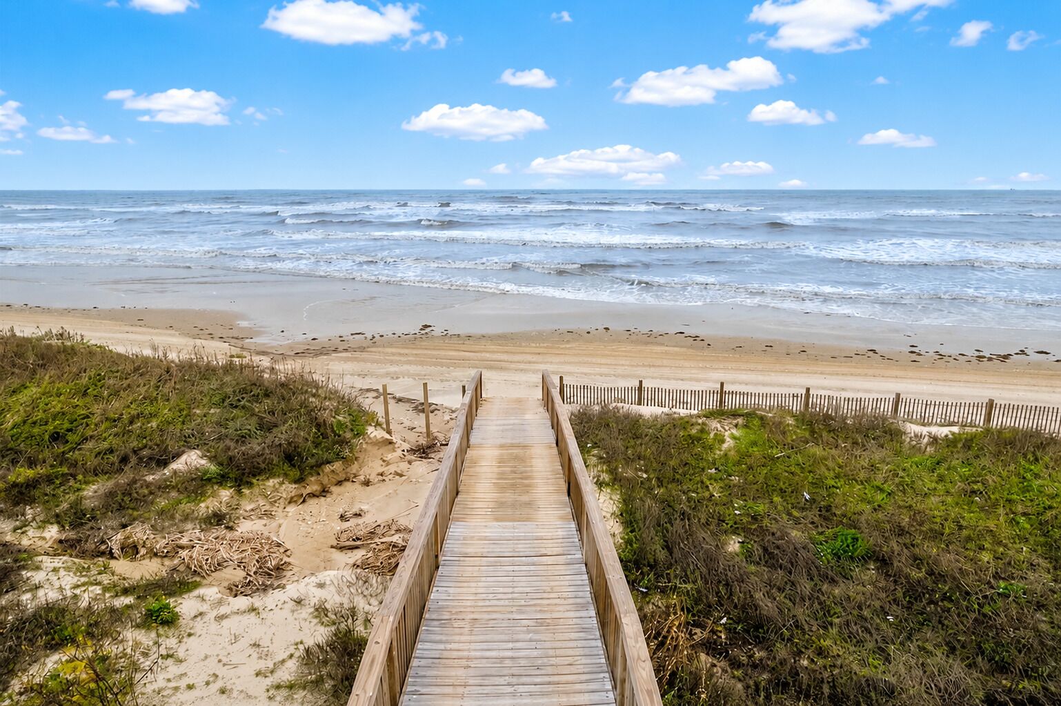 A wooden boardwalk leading to a beach with a sandy shoreline and ocean view.