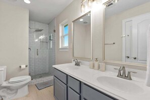 Un bagno con il water bianco, un ampio lavabo con doppio lavandino e una doccia a pavimento con pareti in vetro.