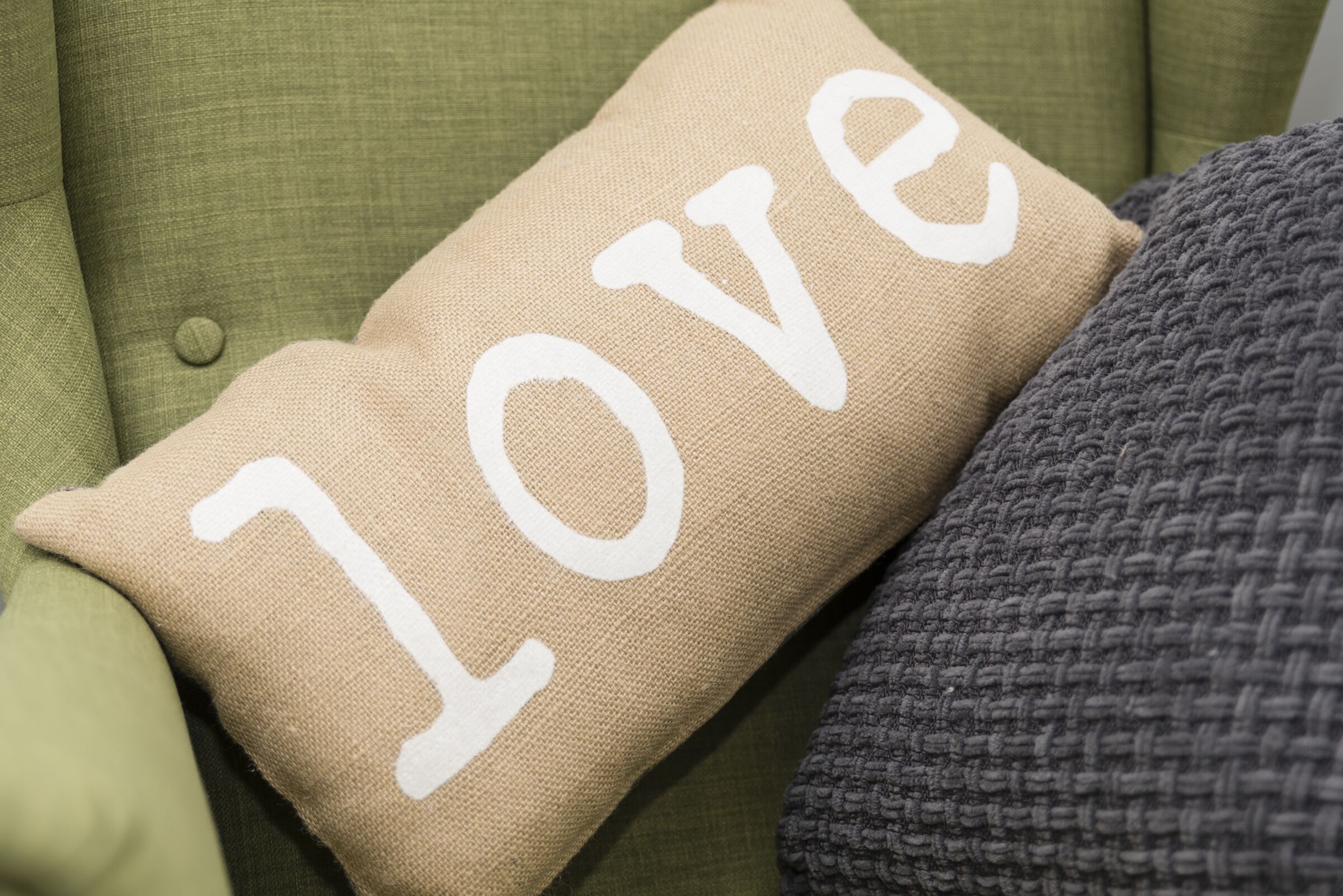 A beige pillow with the word "LOVE" on it, placed on a green couch.