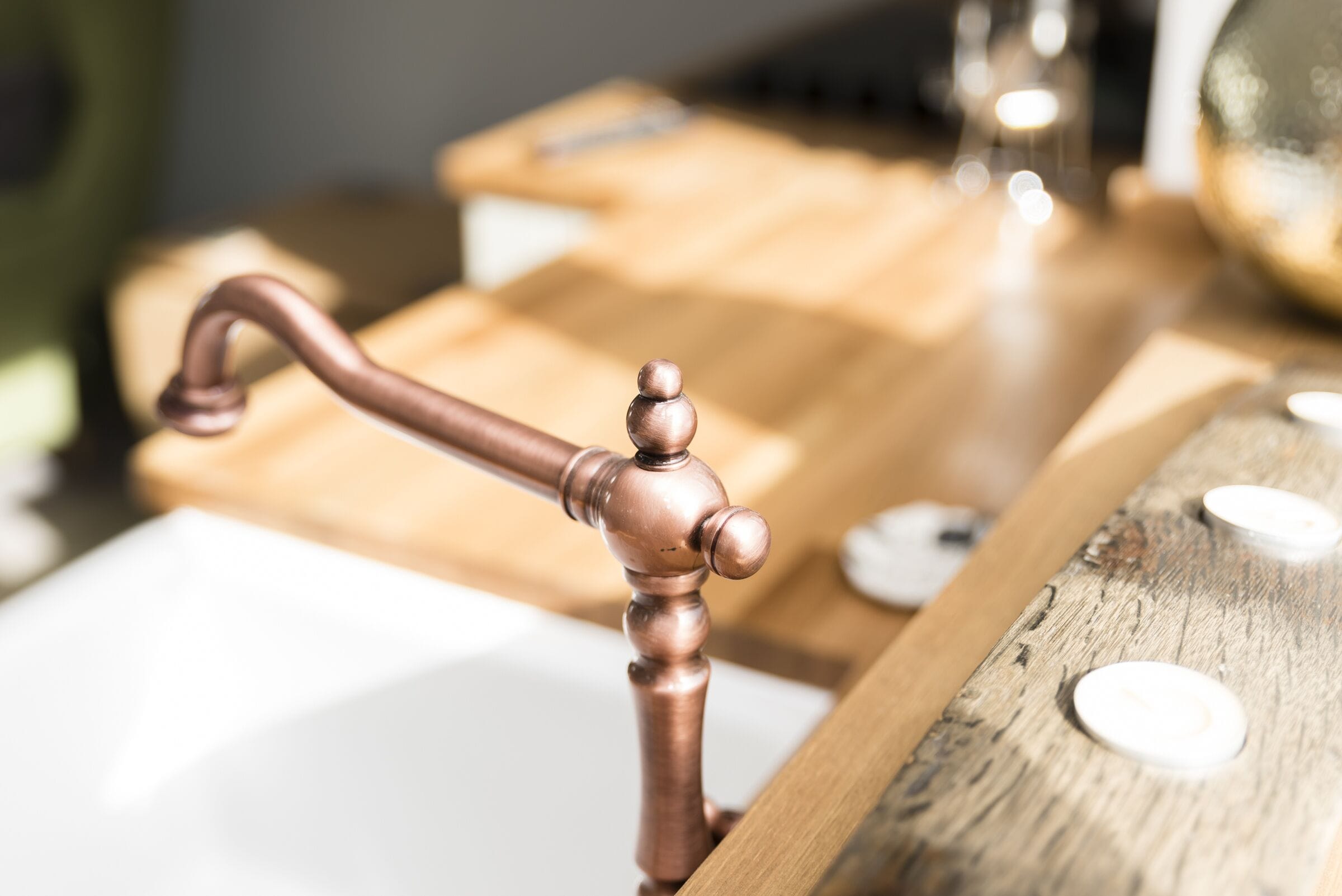 A close-up of a copper faucet with a wooden handle on a wooden surface.