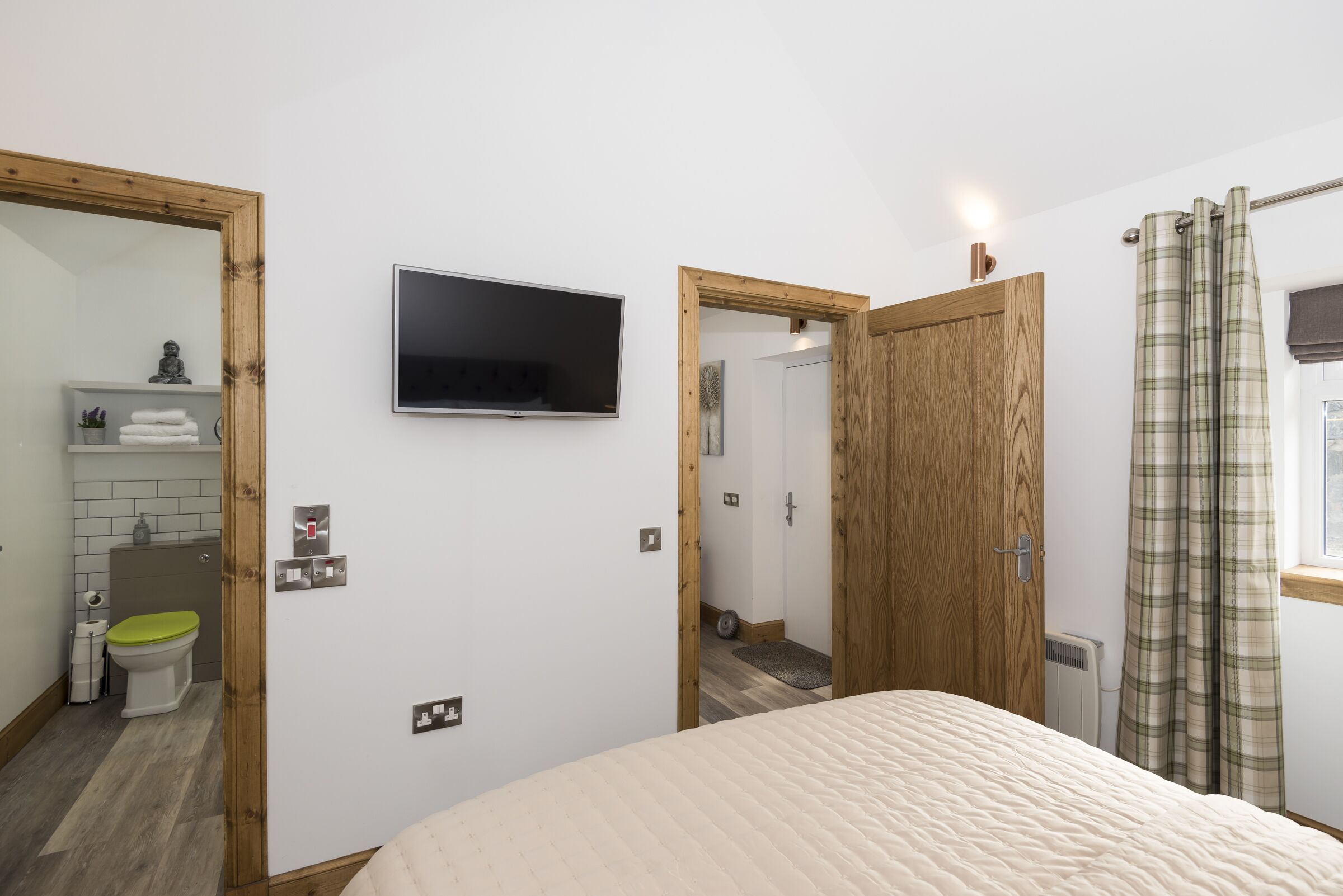 Un dormitorio con una cama, un televisor montado en la pared y una puerta de madera.