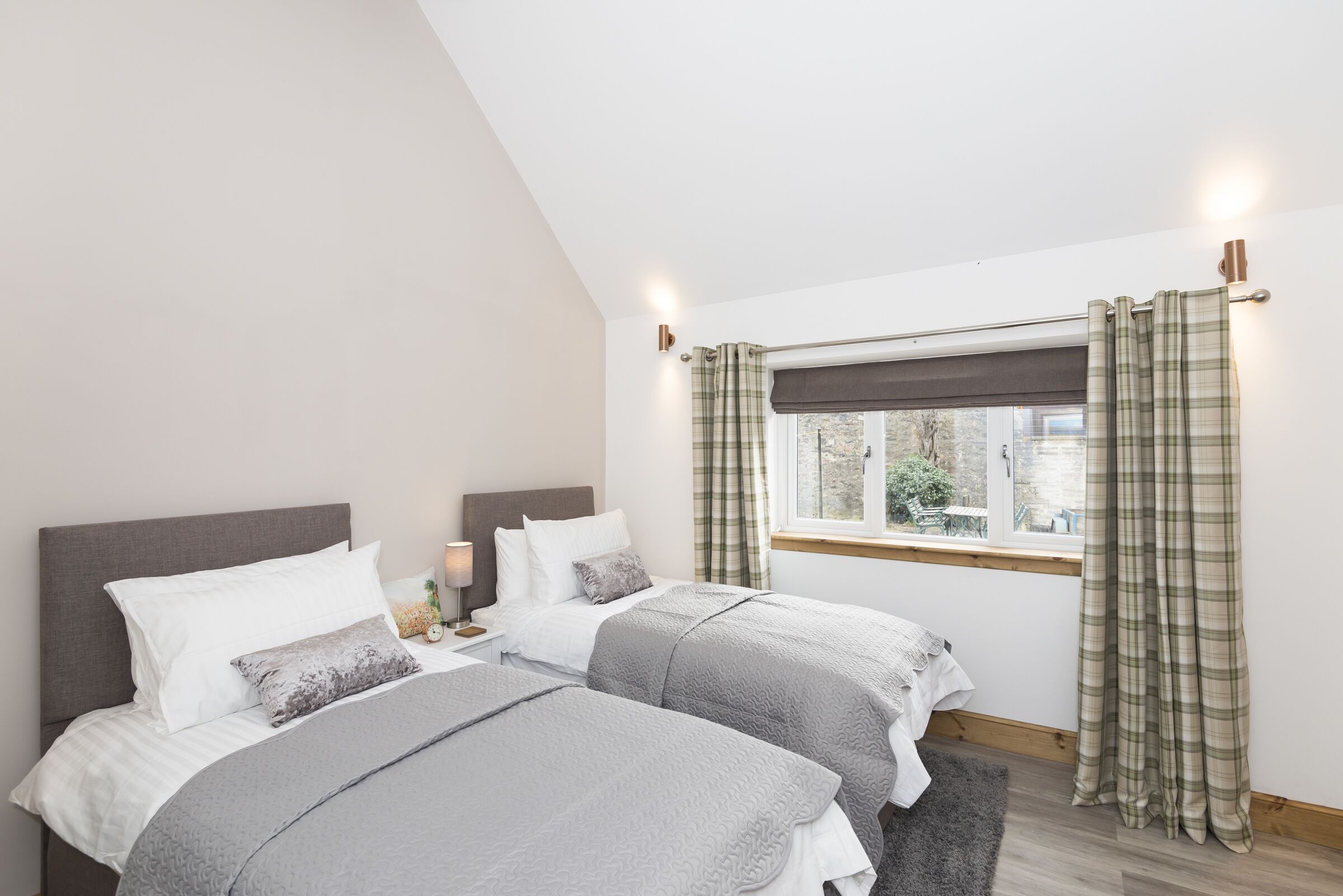 A bedroom with two beds, a window with curtains, and a nightstand with a lamp.