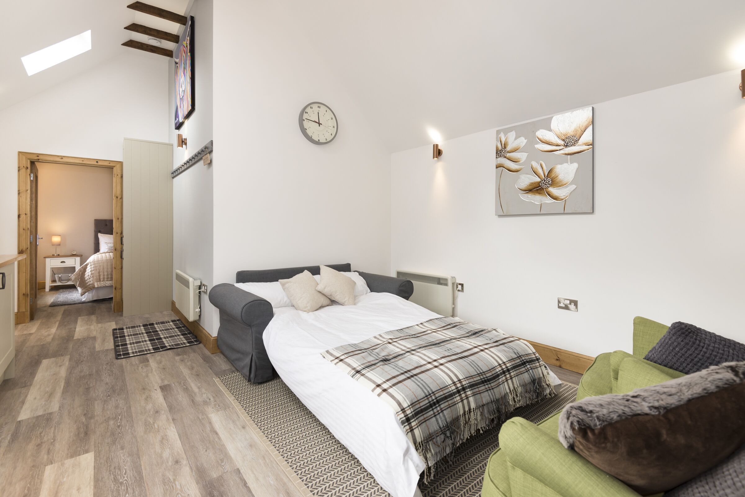 Um quarto moderno com uma cama, um sofá verde, um relógio de parede e uma obra de arte floral.