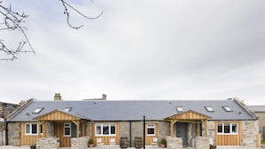 Un bâtiment en pierre doté de deux portes en bois, d’un porche couvert et d’une allée gravillonnée.