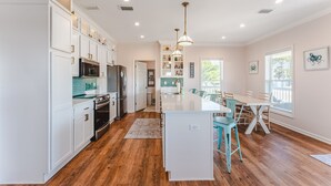 Une cuisine spacieuse avec des meubles blancs, un îlot central et un coin repas doté de chaises de couleur turquoise.
