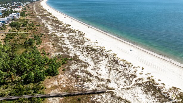 Une plage côtière avec un rivage sablonneux, quelques bâtiments et une voie ferrée qui longe la plage.