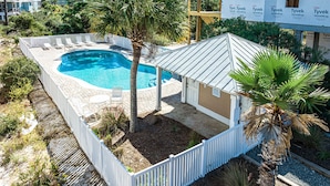 Une piscine dotée d’une terrasse blanche, entourée de palmiers et délimitée par une clôture blanche.