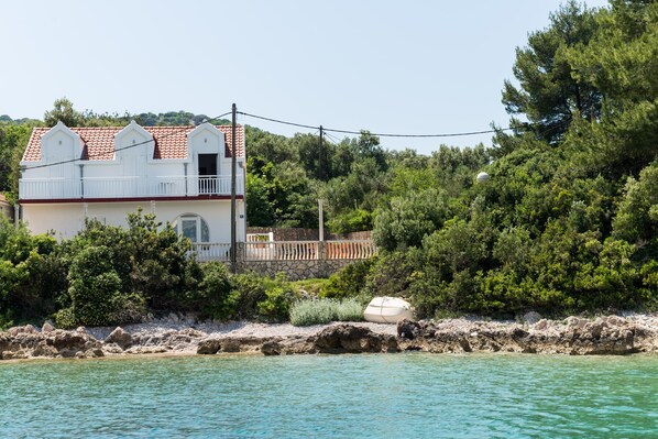 A coastal house with a red-tiled roof, a balcony, and a stone wall.