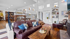 A spacious living room with a leather sofa, wooden coffee table, and a staircase leading to an upper floor. - Spanish Palms | 3BR Home Steps to Windansea Beach (San Diego)