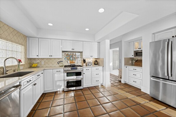 A modern kitchen with white cabinets, stainless steel appliances, and a tiled floor. - Spanish Palms | 3BR Home Steps to Windansea Beach (San Diego)