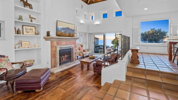 A spacious living room with a fireplace, wooden flooring, and a view of the outdoors. - Spanish Palms | 3BR Home Steps to Windansea Beach (San Diego)