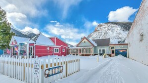 A snow-covered street with buildings, a white picket fence, and a sign indicating a driveway for guests.