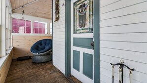 A room with a wooden ceiling, a blue chair, a door with a stained glass window, and a wooden bench.