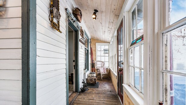 A corridor with wooden flooring, white walls, and large windows.