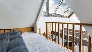 A room with a sloped ceiling, a bed, a wooden railing, and a view of a snowy landscape through a skylight.