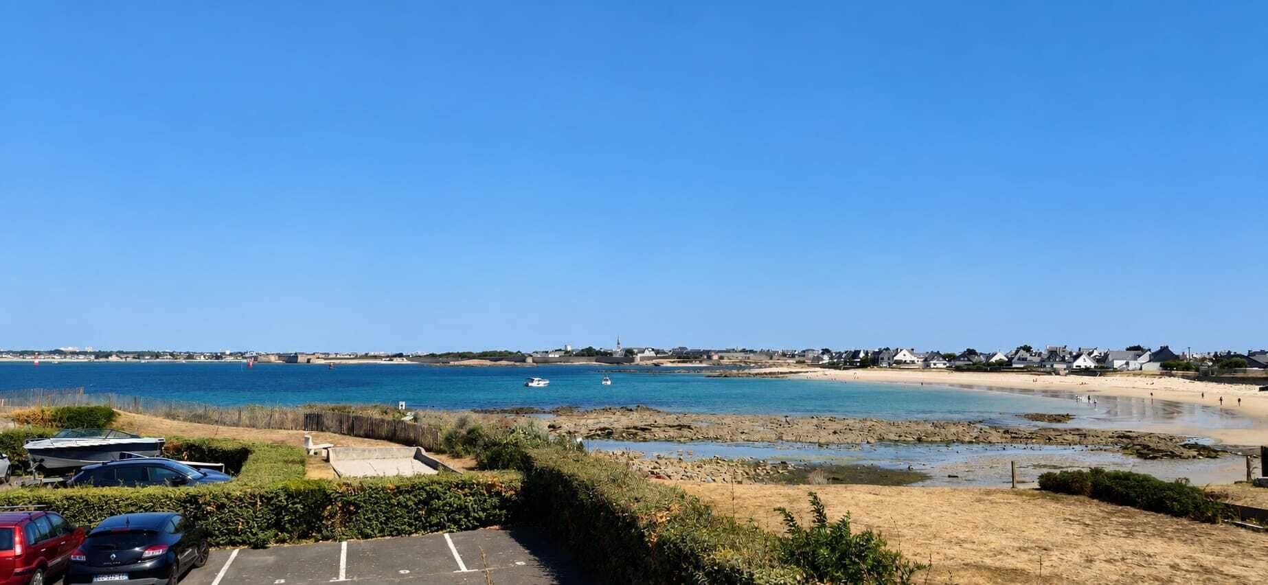 A coastal view with a parking area, beach, and houses in the background.