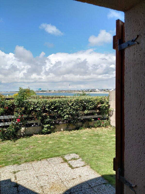 A view from a balcony with a garden, a grassy area, and a body of water in the background. - Idéal Vacances, vue Mer, Accès Direct à la Plage (Gâvres)