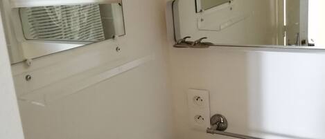 Un baño con un lavamanos blanco, dos espejos, un perchero para toallas e iluminación.