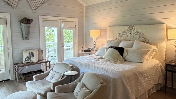 A bedroom with a large bed, two chairs, a ceiling fan, and a window with a view. - Cozy and comfortable one bedroom with kitchen and with pasture view. (Burton)