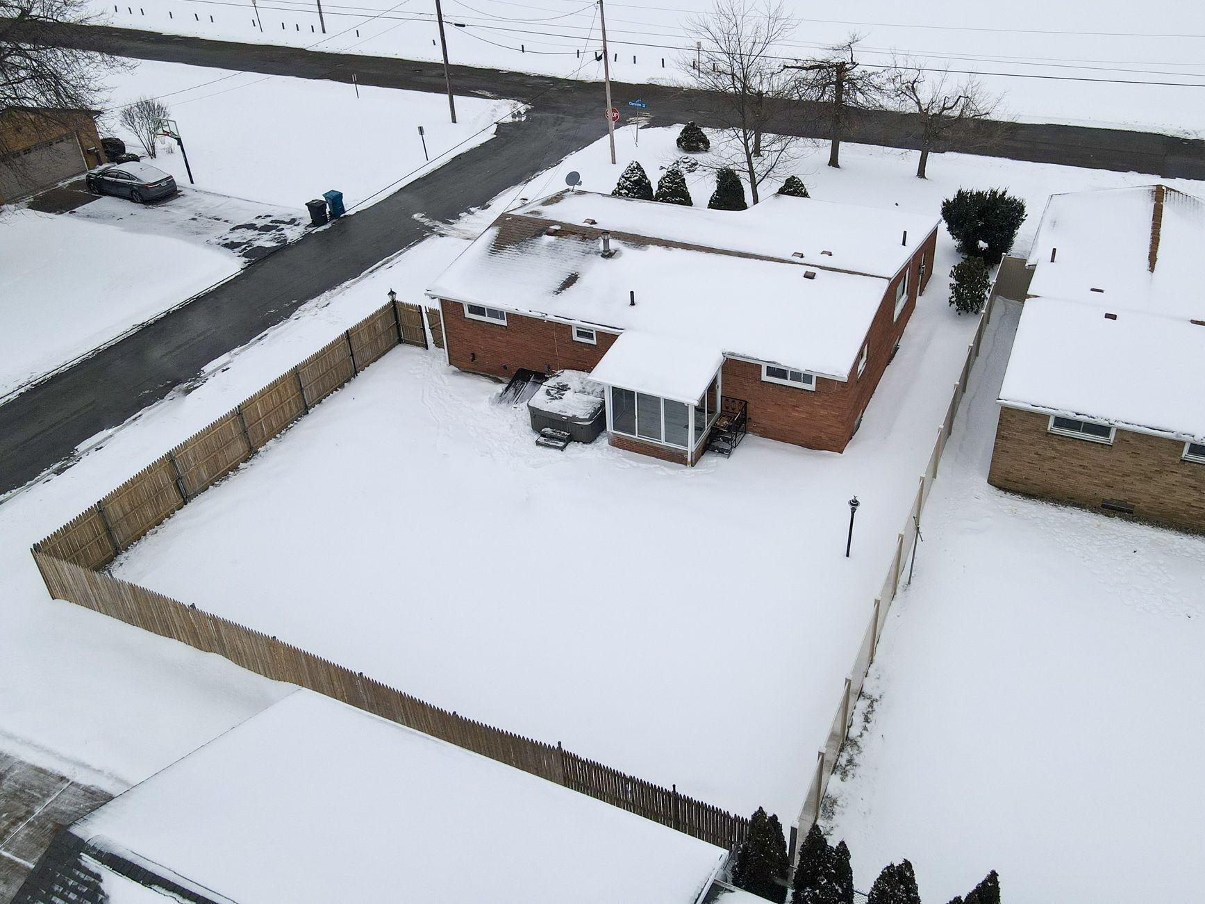 Zona residencial amb una casa de maó, un garatge i un pati tancat cobert de neu.