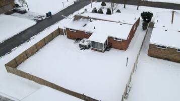 Zona residencial amb una casa de maó, un garatge i un pati tancat cobert de neu.