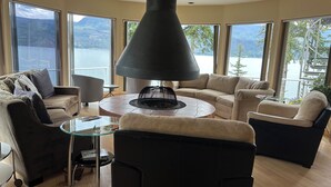 A modern living room with a fireplace, large windows, and a view of a lake and mountains.