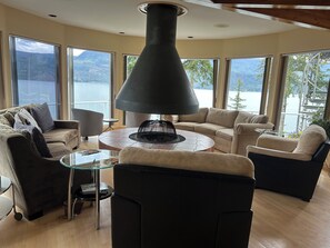 A modern living room with a fireplace, large windows, and a view of a lake and mountains.